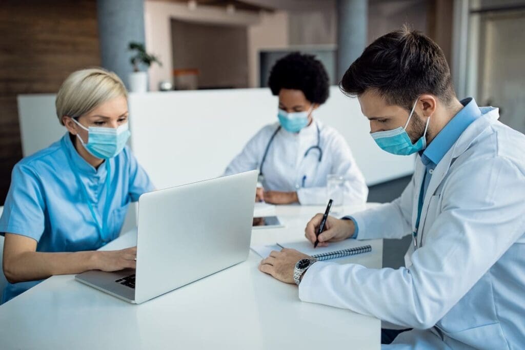 Doctors collaborating at a table with laptops.